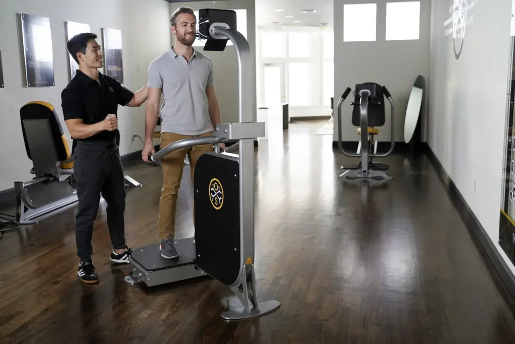 An OsteoStrong coach guiding a member on a Spectrum device in the center